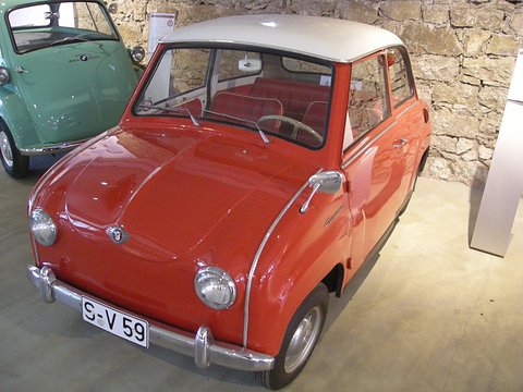 Red saloon with a white roof in front of a stone wall, a green Isetta at the left edge. Opens a larger view