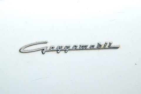 Chrome script badge reading Goggomobil on plain white paint. Opens a larger view