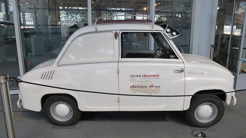 White saloon-based van in side view with signwriting on its panel, in a glass-walled hall. Opens a larger view