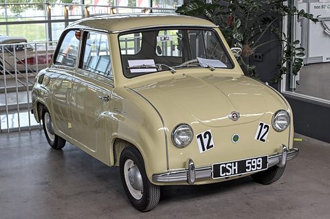 Cream two-door saloon with chrome bumpers and number 12 on its doors, parked in a glass-roofed hall. Opens a larger view