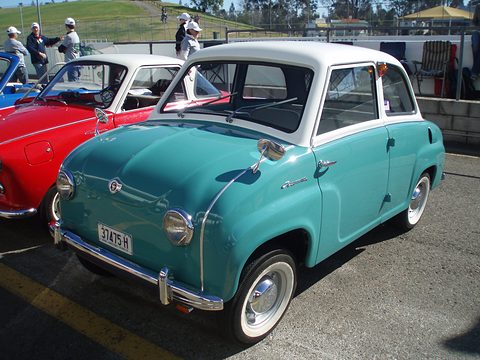 Teal saloon with white roof and whitewall tyres, seen from the front left, other small cars behind. Opens a larger view