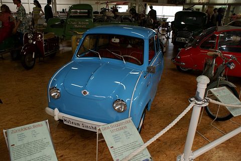 Sky-blue saloon seen head-on behind a rope barrier, information boards in front, other old cars around. Opens a larger view