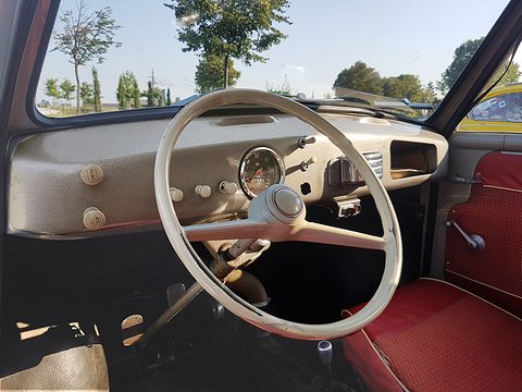 Cream steering wheel in front of a crackle-finish grey dashboard with a central speedometer and pull knobs. Opens a larger view