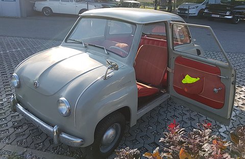 Pale grey saloon with its rear-hinged door open showing red seats, flowers in the foreground. Opens a larger view