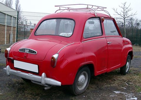 Rear three-quarter view of a red saloon with a roof rack and louvred engine lid, by a fence. Opens a larger view