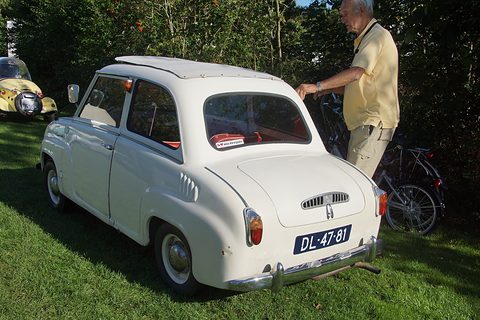 White saloon on grass seen from behind on the left, a man leaning on the open door. Opens a larger view