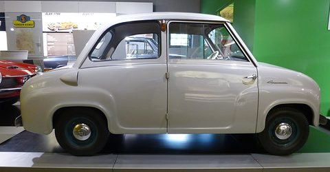 Pale grey saloon in side profile on a museum plinth, against a green wall with old Glas posters