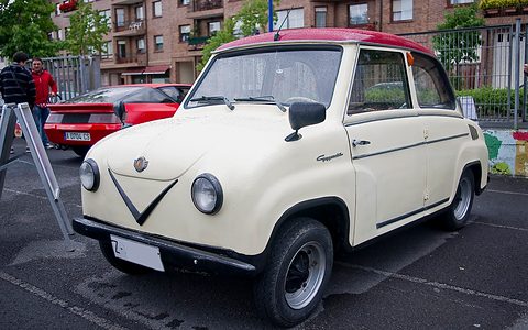 Cream saloon with a maroon roof parked on a wet car park, seen from the front left. Opens a larger view