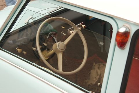 View through the side window of a large cream two-spoke steering wheel and a plain painted dashboard. Opens a larger view
