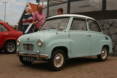 Pale green saloon with whitewall tyres on brick paving, seen from the front left, a red car beside it. Opens a larger view
