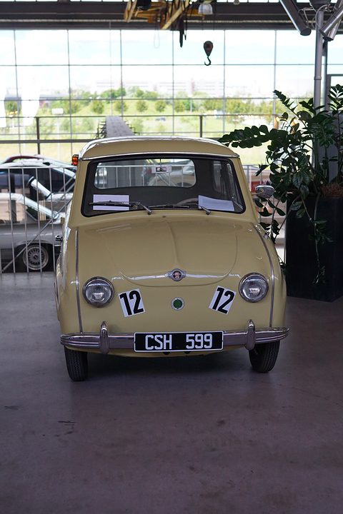 Cream saloon seen straight from the front, round headlamps, number 12 on the bonnet, under a glass hall roof. Opens a larger view
