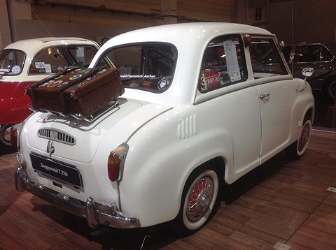 Rear of a white saloon with a brown leather suitcase on a rack above the louvred engine lid. Opens a larger view