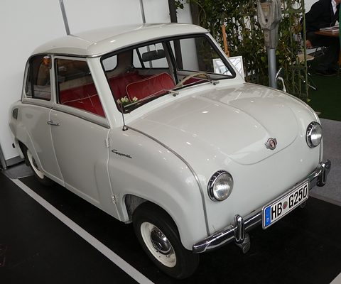 White saloon with red seats on a show floor, seen from the front right. Opens a larger view