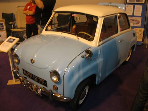 Pale blue saloon with cream roof on a purple carpet, seen from the front right, display boards behind. Opens a larger view