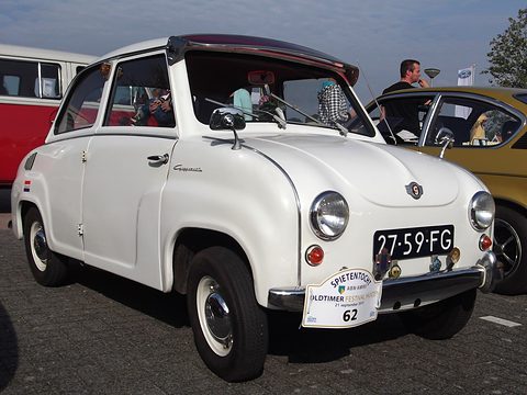 White saloon with an open fabric sunroof and a rally plate on its bumper, seen from the front left. Opens a larger view