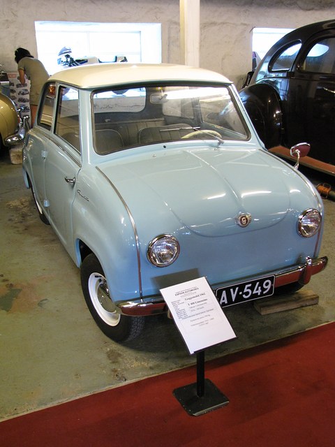 Pale blue saloon on a red museum floor with a caption stand in front, seen from the front left. Opens a larger view