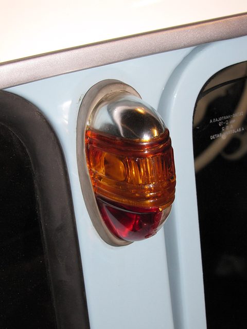 Close-up of an amber and red oval indicator lamp on pale blue bodywork beside a window. Opens a larger view