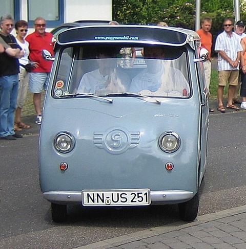 Grey van with two occupants driving towards the camera, spectators beside the road