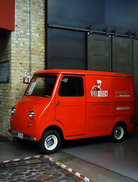 Red panel van with modern courier lettering parked by a brick wall in an old depot