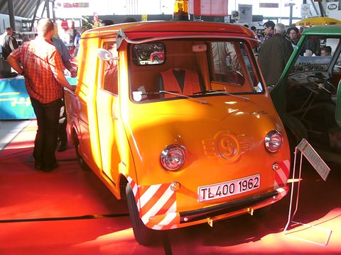 Orange pick-up with red and white striped bumper ends, seen from the front in a show hall