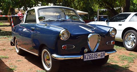 Dark blue coupé with a white roof on red earth, seen from the front left. Opens a larger view