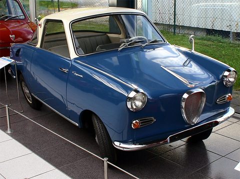 Dark blue coupé with a cream roof on a tiled floor, seen from the front right. Opens a larger view