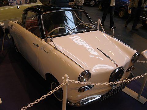 Cream coupé with a black roof behind a chain barrier on a show carpet. Opens a larger view