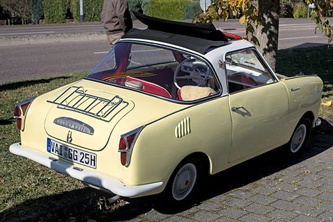 Rear three-quarter of a cream coupé with an open fabric roof and a chrome rack on its tail. Opens a larger view