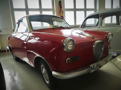 Dark red coupé with chrome trim close up in a museum hall with tall windows. Opens a larger view