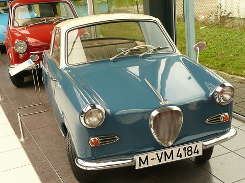 Blue coupé with a cream roof and shield grille on a tiled floor, another coupé behind. Opens a larger view