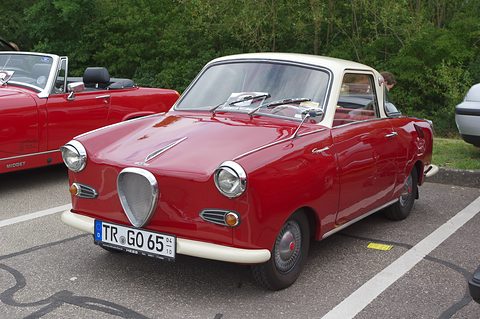 Dark red coupé with a cream roof parked on tarmac, seen from the front left. Opens a larger view