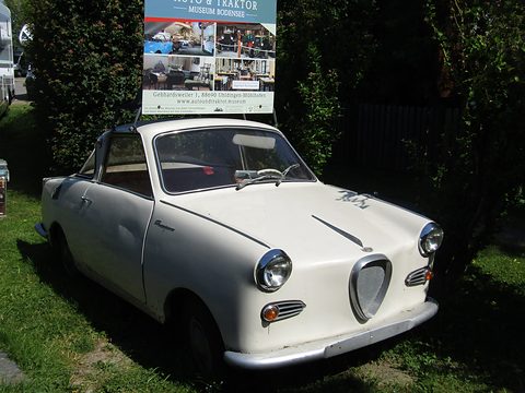 White coupé seen from the front left on a lawn, a museum sign board behind. Opens a larger view