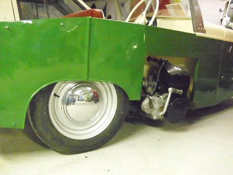 Green body side with a white wheel and a bare single-cylinder engine bolted on outside it. Opens a larger view