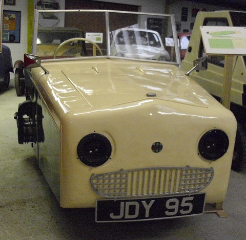 Cream bonnet and green flank of a boxy open three-wheeler, its engine sticking out at the side. Opens a larger view