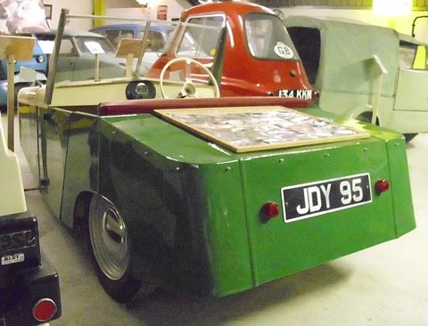 Green rear of a boxy three-wheeler with plate JDY 95 and a framed photo display on the boot. Opens a larger view
