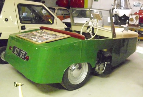 Green rear quarter of a three-wheeler with a white wheel and an engine mounted outside the body.