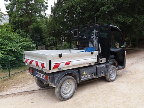 Rear of a black electric utility truck with a white tipper bed and red and white stripes on a sandy path. Opens a larger view