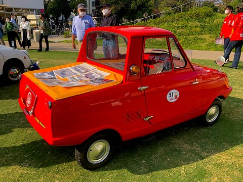 Rear three-quarter of a red pickup whose short load bed is covered with an orange cloth and leaflets.