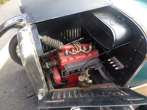 Open bonnet panel revealing a red four-cylinder engine with polished pipes in a teal car. Opens a larger view