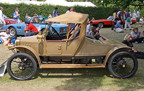 Beige two-seater with a tan hood and black wire wheels in profile on grass, spectators sitting behind.