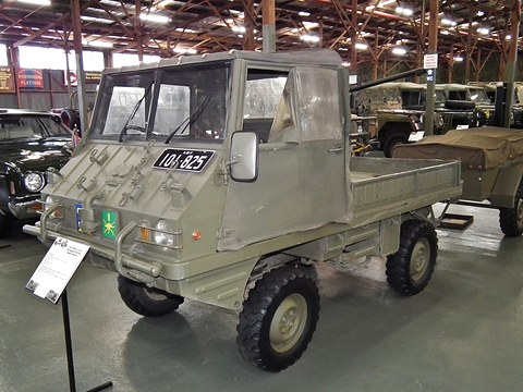 Olive small 4x4 with a soft-top cab and army number plate in a long museum shed.