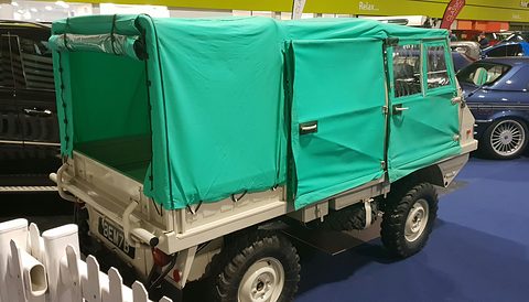 Small 4x4 with a bright green canvas tilt and white bodywork on a show stand. Opens a larger view