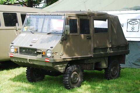 Olive small 4x4 with a full canvas cab on grass in front of a white tent. Opens a larger view