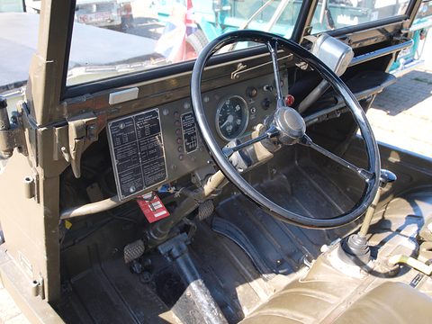 Large steering wheel, gauge and metal data plates on the dashboard of a small military 4x4. Opens a larger view