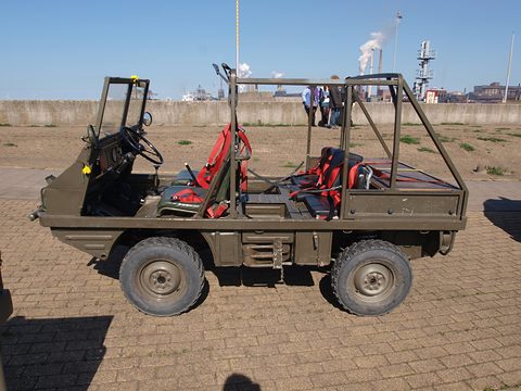Side view of a small open olive 4x4 with roll bars and red racing seats on brick paving. Opens a larger view
