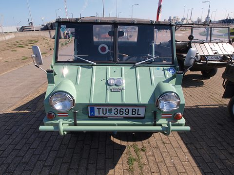 Front of a pale green small 4x4 with large round sealed-beam headlamps and an Austrian plate. Opens a larger view