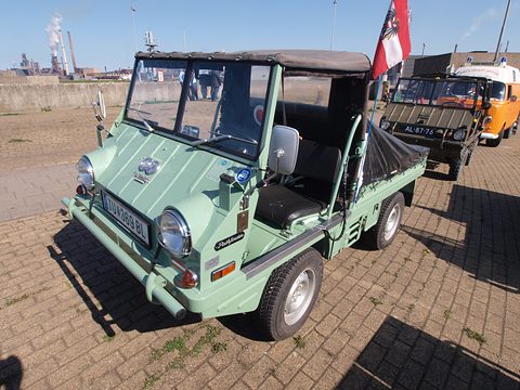Pale green small 4x4 with large headlamps, a soft top and a flag, parked on brick paving. Opens a larger view
