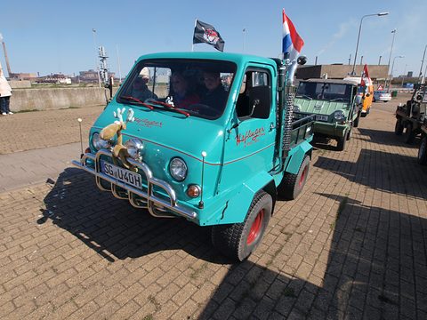 Turquoise small truck with a rounded plastic cab, flags and red wheels on brick paving. Opens a larger view