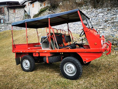 Red small 4x4 with a black canopy and bench seats on a grassy slope by a stone wall. Opens a larger view