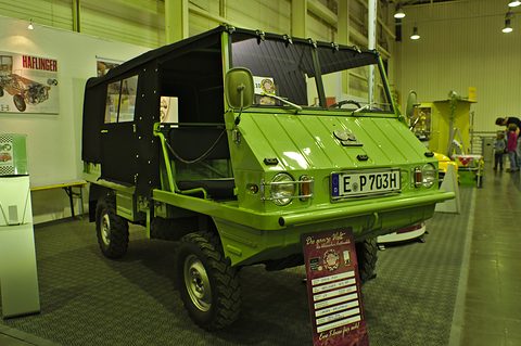 Lime-green small 4x4 with a black canvas cab on a show stand, an information board in front. Opens a larger view